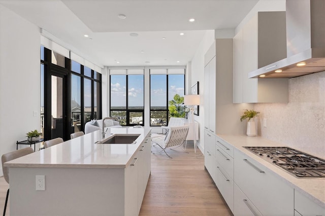 kitchen featuring wall chimney range hood, a sink, modern cabinets, stainless steel gas cooktop, and white cabinetry