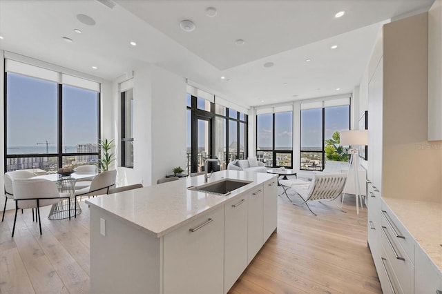 kitchen with a sink, a wall of windows, light wood finished floors, white cabinets, and open floor plan