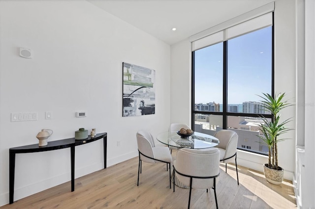 dining area featuring wood finished floors, a wall of windows, baseboards, and a city view