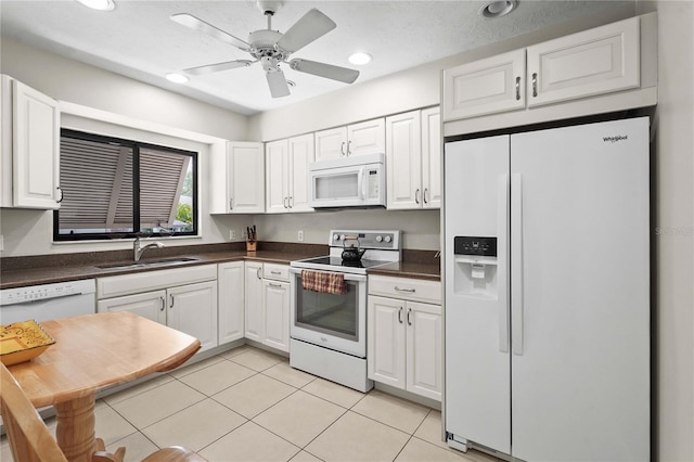 kitchen featuring white appliances, a sink, dark countertops, white cabinets, and recessed lighting