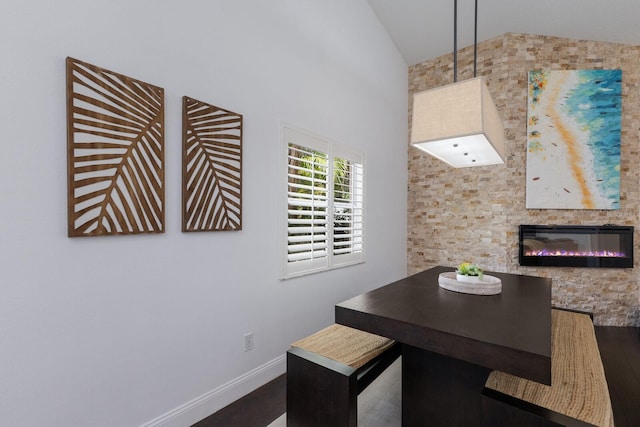 dining space with a glass covered fireplace, baseboards, vaulted ceiling, and dark wood-type flooring