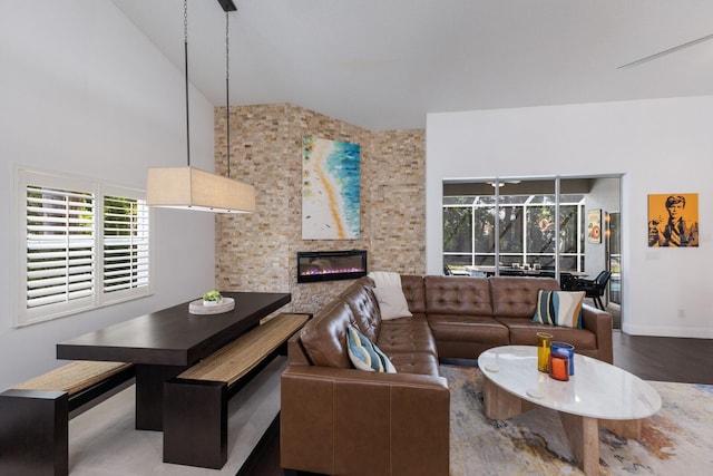 living room featuring high vaulted ceiling, a glass covered fireplace, a healthy amount of sunlight, and wood finished floors