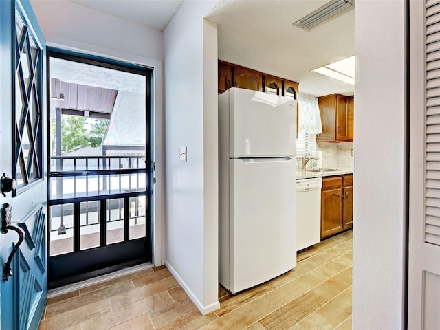 kitchen featuring brown cabinets, light wood-type flooring, light countertops, a sink, and white appliances