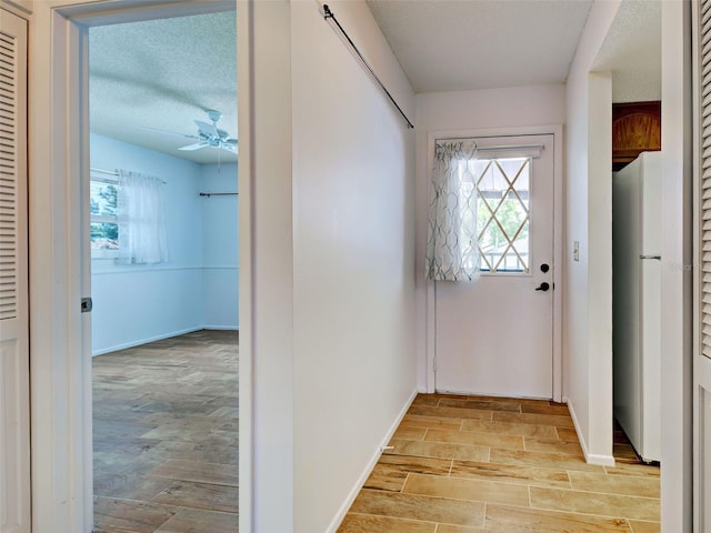 entryway featuring light wood-style floors, a textured ceiling, baseboards, and ceiling fan