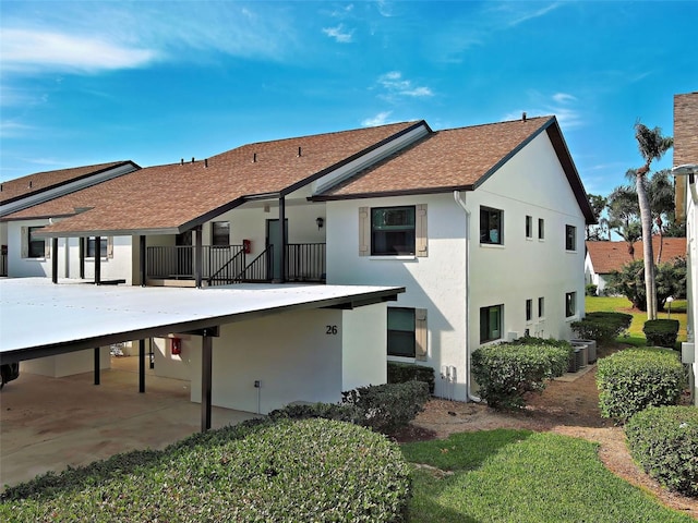 back of house with central AC, stucco siding, an attached carport, a shingled roof, and driveway