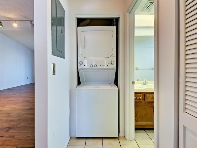 laundry room featuring electric panel, laundry area, stacked washer / dryer, visible vents, and light tile patterned flooring
