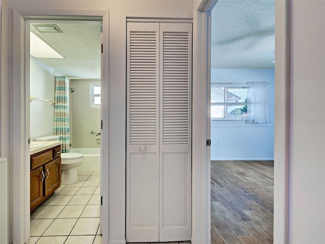 corridor with a textured ceiling, visible vents, and light wood finished floors