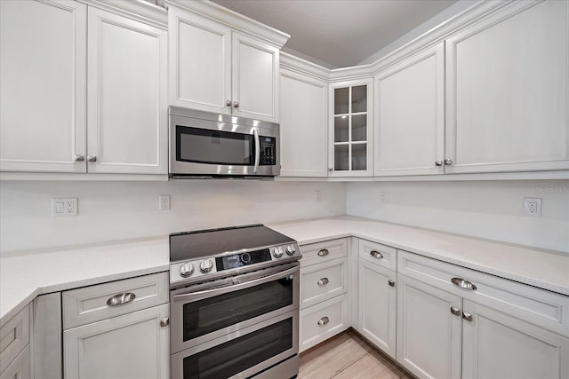 555 N Orange Ave Unit 307, Sarasota, FL 34236 - kitchen featuring appliances with stainless steel finishes, light countertops, white cabinets, and glass insert cabinets
