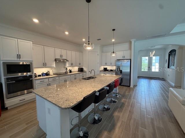 kitchen with a sink, stainless steel appliances, dark wood-type flooring, arched walkways, and under cabinet range hood
