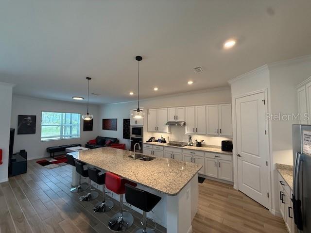 kitchen featuring stainless steel microwave, a sink, white cabinetry, wood finished floors, and black electric cooktop