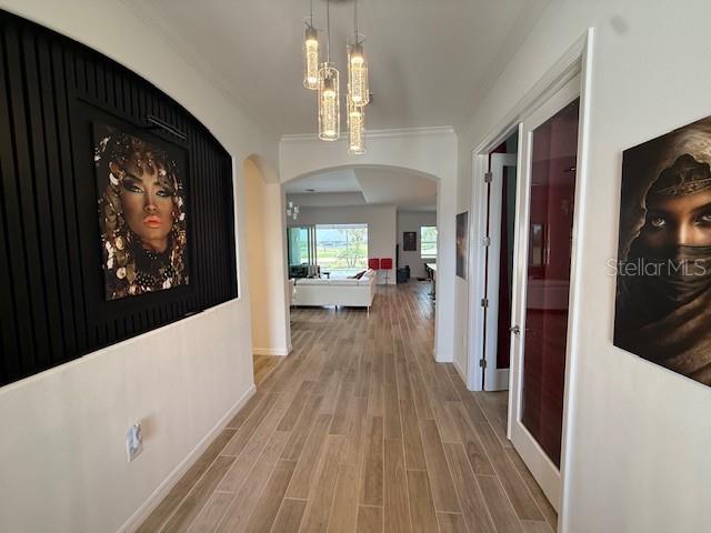 corridor featuring crown molding, arched walkways, light wood-type flooring, and baseboards