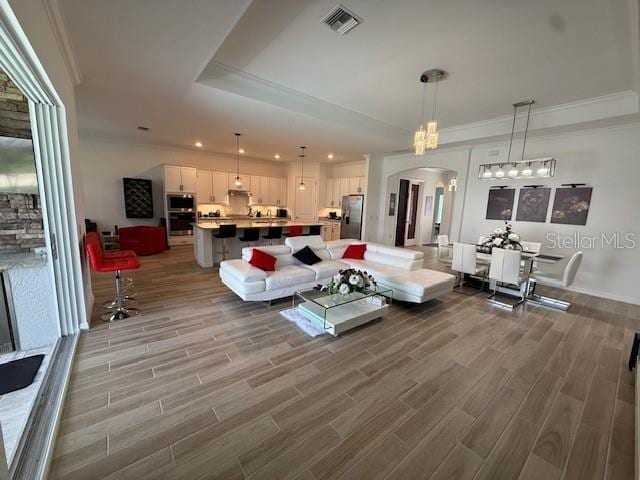 living room featuring a tray ceiling, recessed lighting, visible vents, wood finished floors, and arched walkways