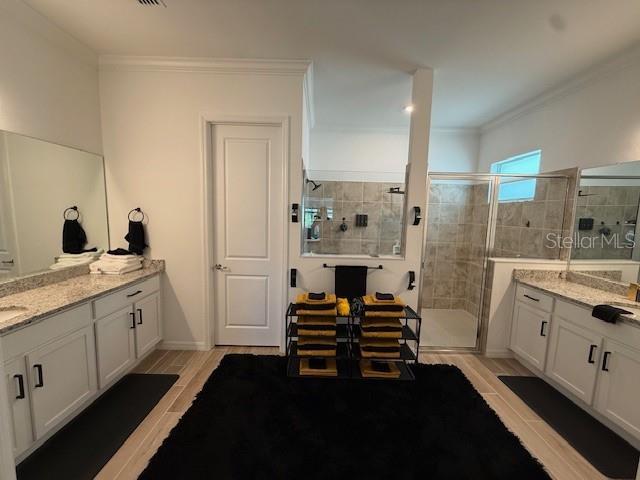 bathroom with a shower stall, ornamental molding, two vanities, and wood finished floors