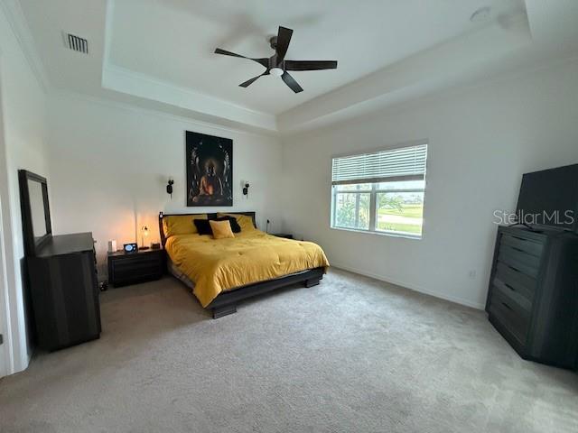 bedroom with a tray ceiling, visible vents, ceiling fan, and light colored carpet