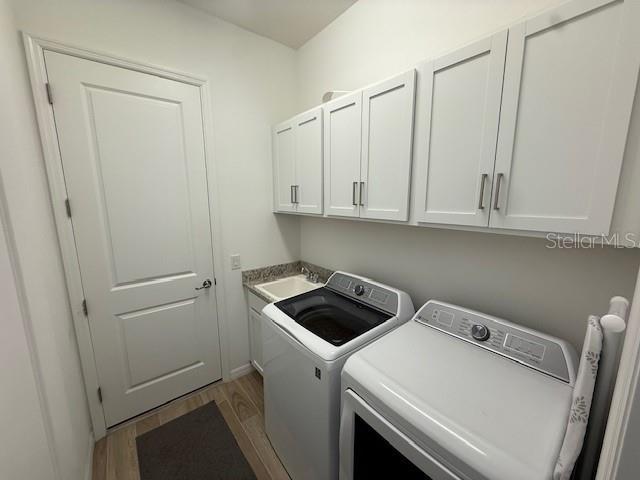 washroom featuring washer and clothes dryer, cabinet space, a sink, and wood finished floors