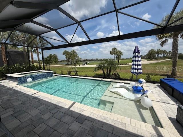 view of pool with a pool with connected hot tub, a patio area, and glass enclosure