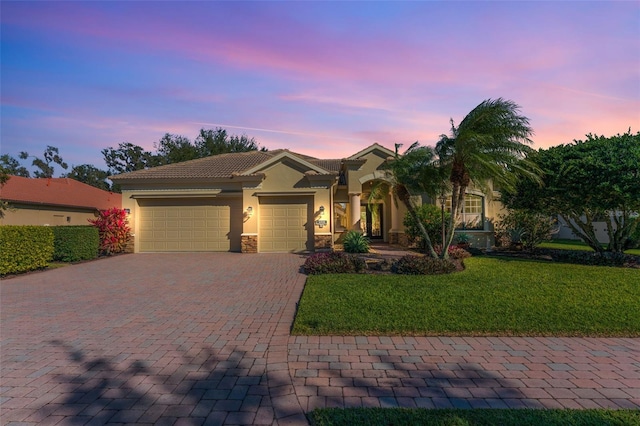 mediterranean / spanish house featuring a lawn, decorative driveway, stucco siding, a tiled roof, and an attached garage