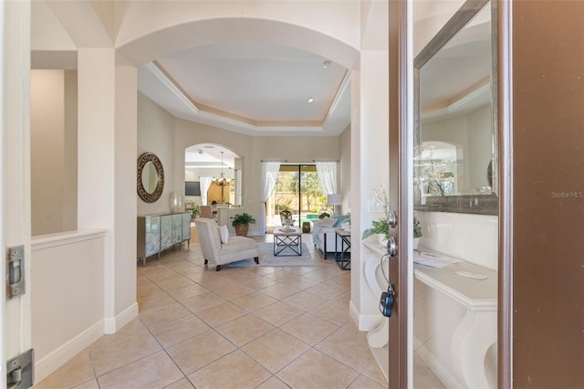 entryway featuring light tile patterned flooring, baseboards, a chandelier, a tray ceiling, and arched walkways