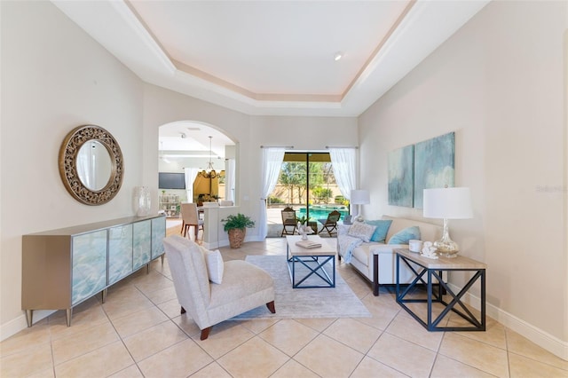 living room featuring arched walkways, light tile patterned floors, baseboards, a notable chandelier, and a tray ceiling