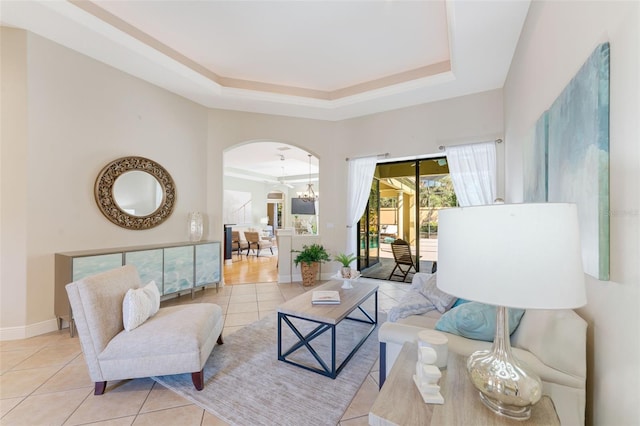 living area with arched walkways, tile patterned flooring, baseboards, a chandelier, and a tray ceiling