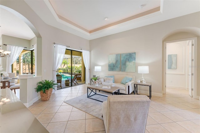 living room with light tile patterned floors, arched walkways, baseboards, and a tray ceiling
