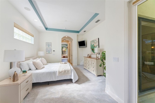 bedroom featuring visible vents, light carpet, baseboards, a raised ceiling, and arched walkways