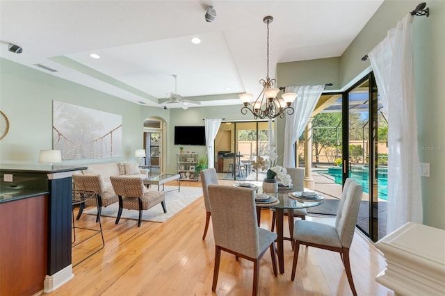 dining space featuring a raised ceiling, arched walkways, ceiling fan with notable chandelier, light wood-type flooring, and visible vents