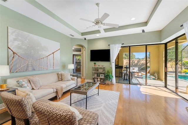 living room with arched walkways, a ceiling fan, a raised ceiling, and hardwood / wood-style floors