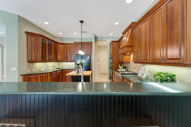 kitchen featuring glass insert cabinets, premium range hood, recessed lighting, arched walkways, and black fridge