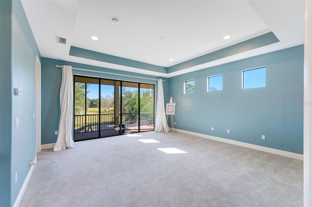 carpeted spare room featuring recessed lighting, a tray ceiling, visible vents, and baseboards