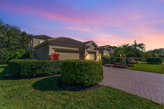 mediterranean / spanish home featuring a garage, stucco siding, a lawn, a tiled roof, and driveway