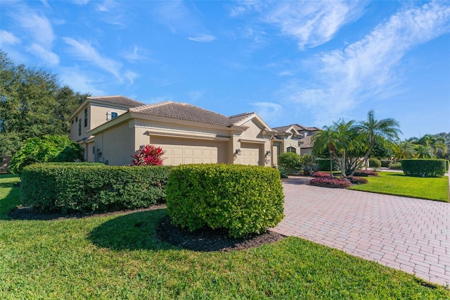 mediterranean / spanish house featuring driveway, a tile roof, a front yard, a garage, and stucco siding