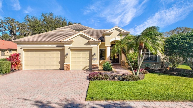mediterranean / spanish-style home featuring an attached garage, stone siding, stucco siding, a front yard, and decorative driveway
