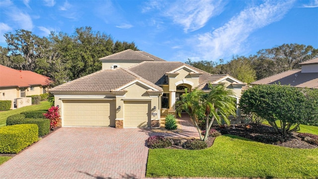mediterranean / spanish-style house with an attached garage, a front lawn, a tile roof, stucco siding, and decorative driveway
