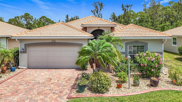 mediterranean / spanish house with stucco siding, a tiled roof, an attached garage, and decorative driveway