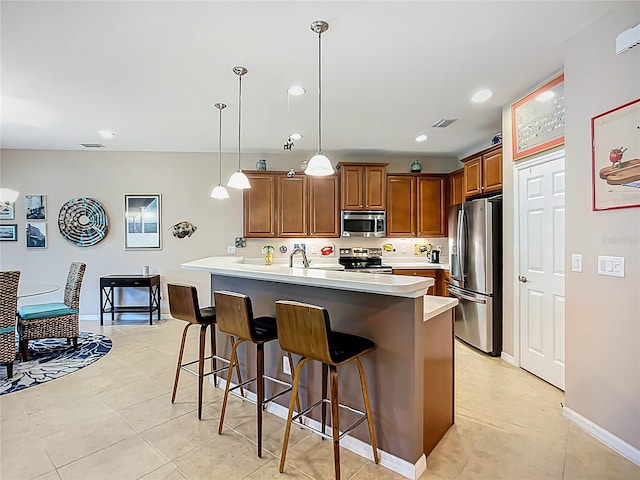 kitchen with appliances with stainless steel finishes, a breakfast bar area, brown cabinets, light countertops, and pendant lighting