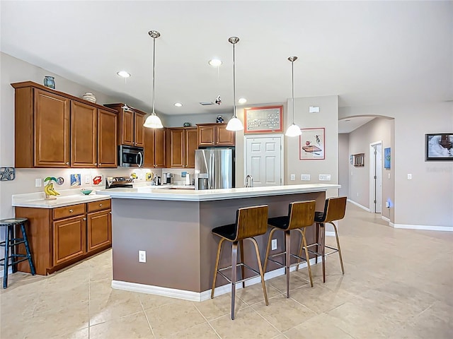kitchen with stainless steel appliances, a kitchen breakfast bar, arched walkways, brown cabinetry, and recessed lighting