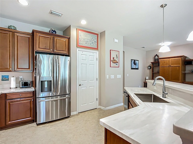 kitchen featuring stainless steel appliances, a sink, light countertops, brown cabinets, and hanging light fixtures