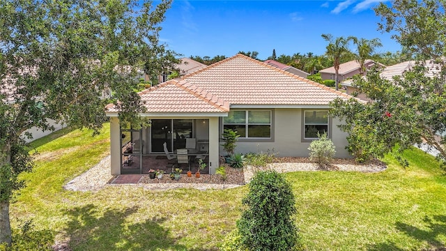 back of property featuring a sunroom, a tiled roof, stucco siding, and a lawn