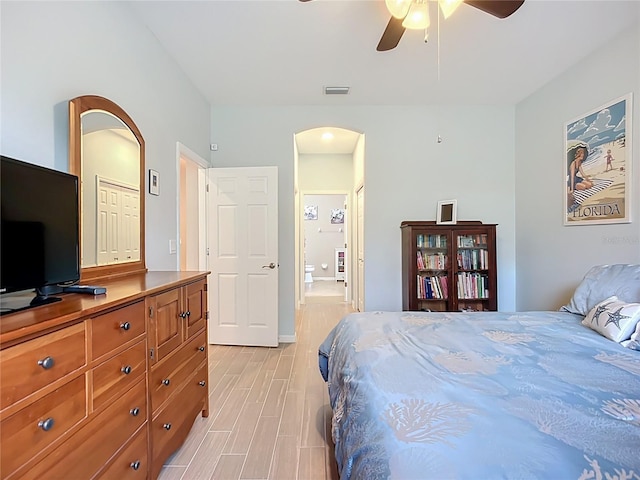bedroom with arched walkways, light wood-style floors, a ceiling fan, and baseboards