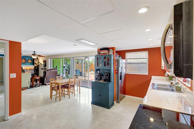 kitchen featuring a sink, stainless steel fridge with ice dispenser, tile countertops, baseboards, and stovetop