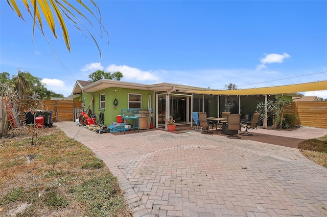 rear view of house featuring fence, stucco siding, a sunroom, a gate, and a patio area