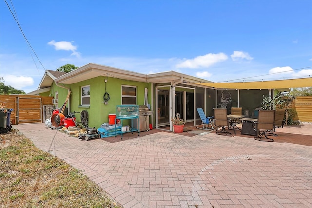 rear view of house with fence, stucco siding, a sunroom, a gate, and a patio