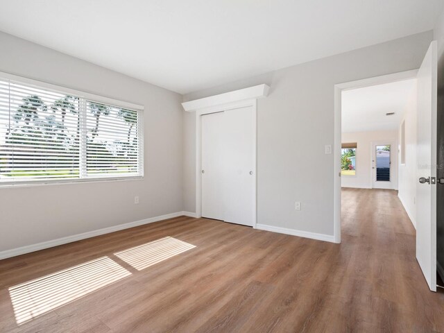 6116 Rodgers Ave, Sarasota, FL 34231 - unfurnished bedroom with baseboards, multiple windows, a closet, and wood finished floors