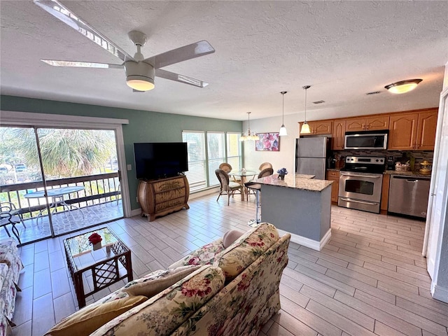 living room with a textured ceiling, baseboards, light wood-style flooring, and ceiling fan