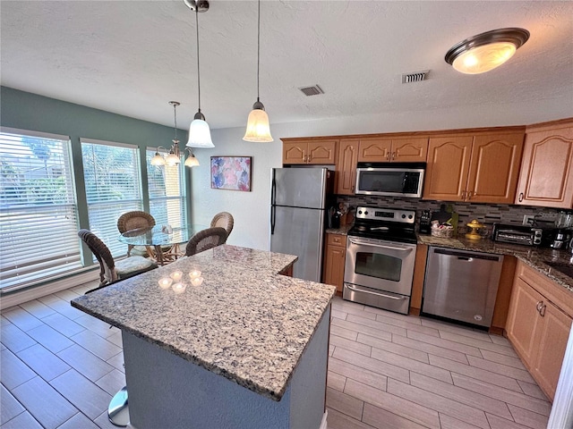 kitchen with light stone counters, visible vents, a kitchen island, backsplash, and stainless steel appliances