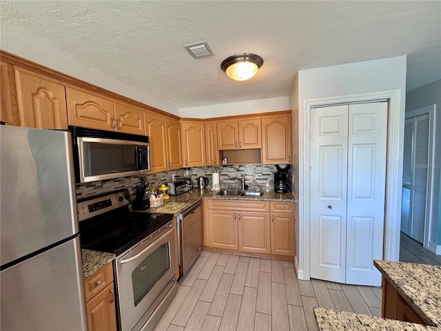 kitchen with visible vents, a sink, wood finish floors, backsplash, and appliances with stainless steel finishes