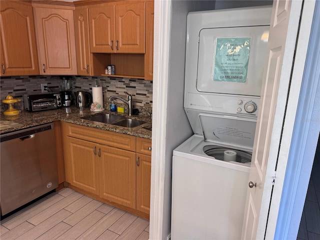 clothes washing area with stacked washer and dryer, light wood finished floors, and a sink