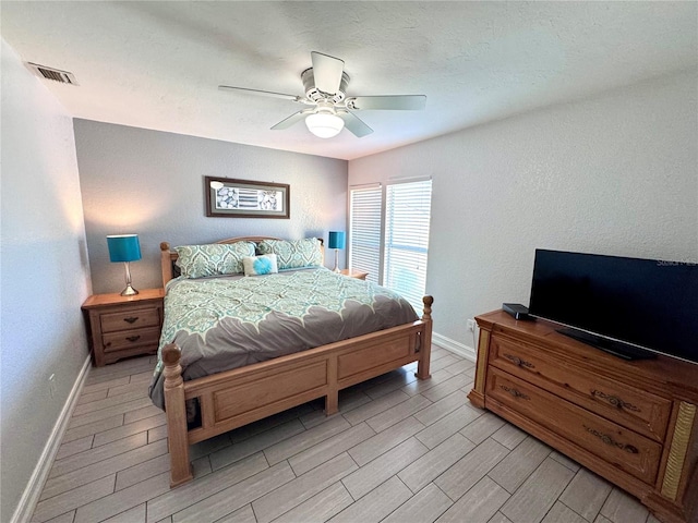 bedroom featuring visible vents, ceiling fan, a textured wall, wood tiled floor, and baseboards