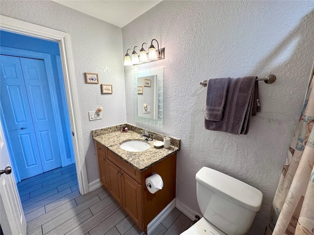 bathroom featuring toilet, vanity, a textured wall, wood tiled floor, and baseboards